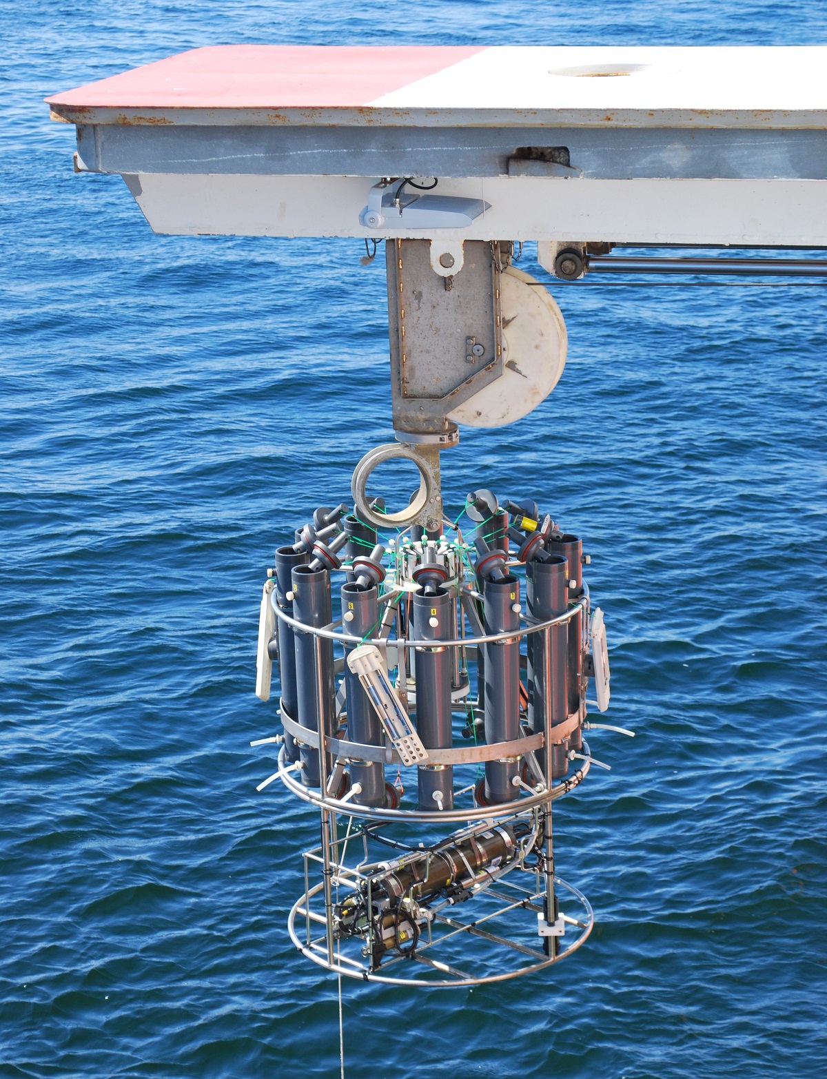 Ett cylinder ramverk med sampel tuber hissas ner med en vinsch ovanpå vatten.