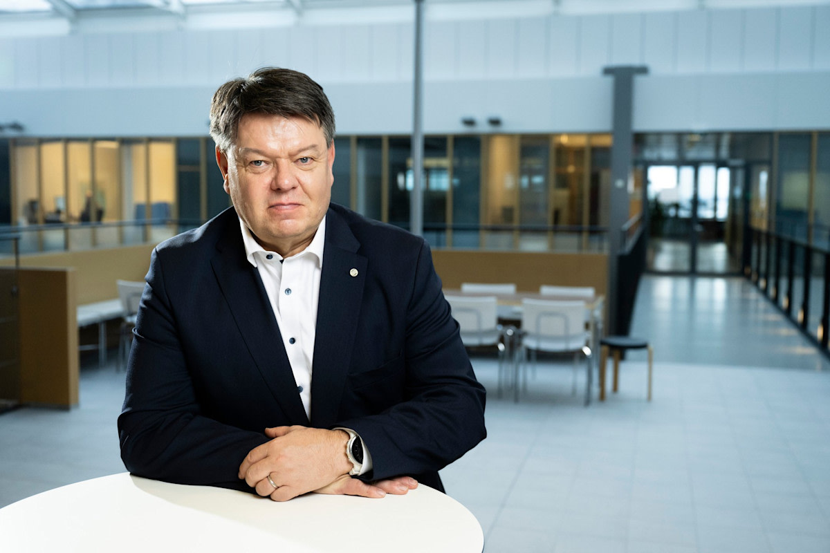 Personen tittar på kameran, håller händerna på bordet. Bilden är tagen inomhus.