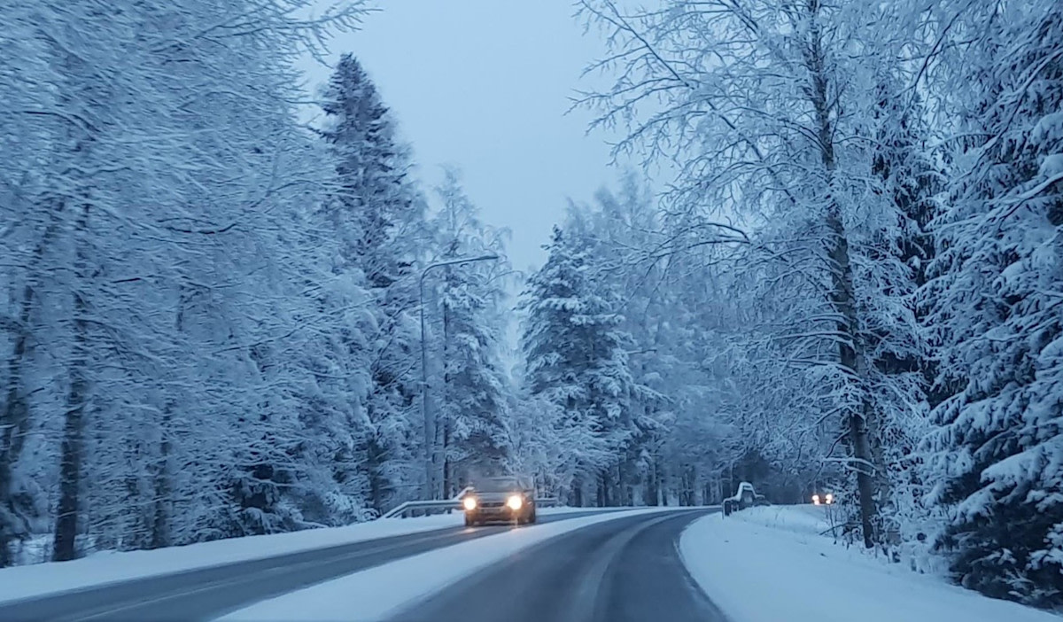 Fotografi av en snötäckt väg som slingrar sig genom en skog.