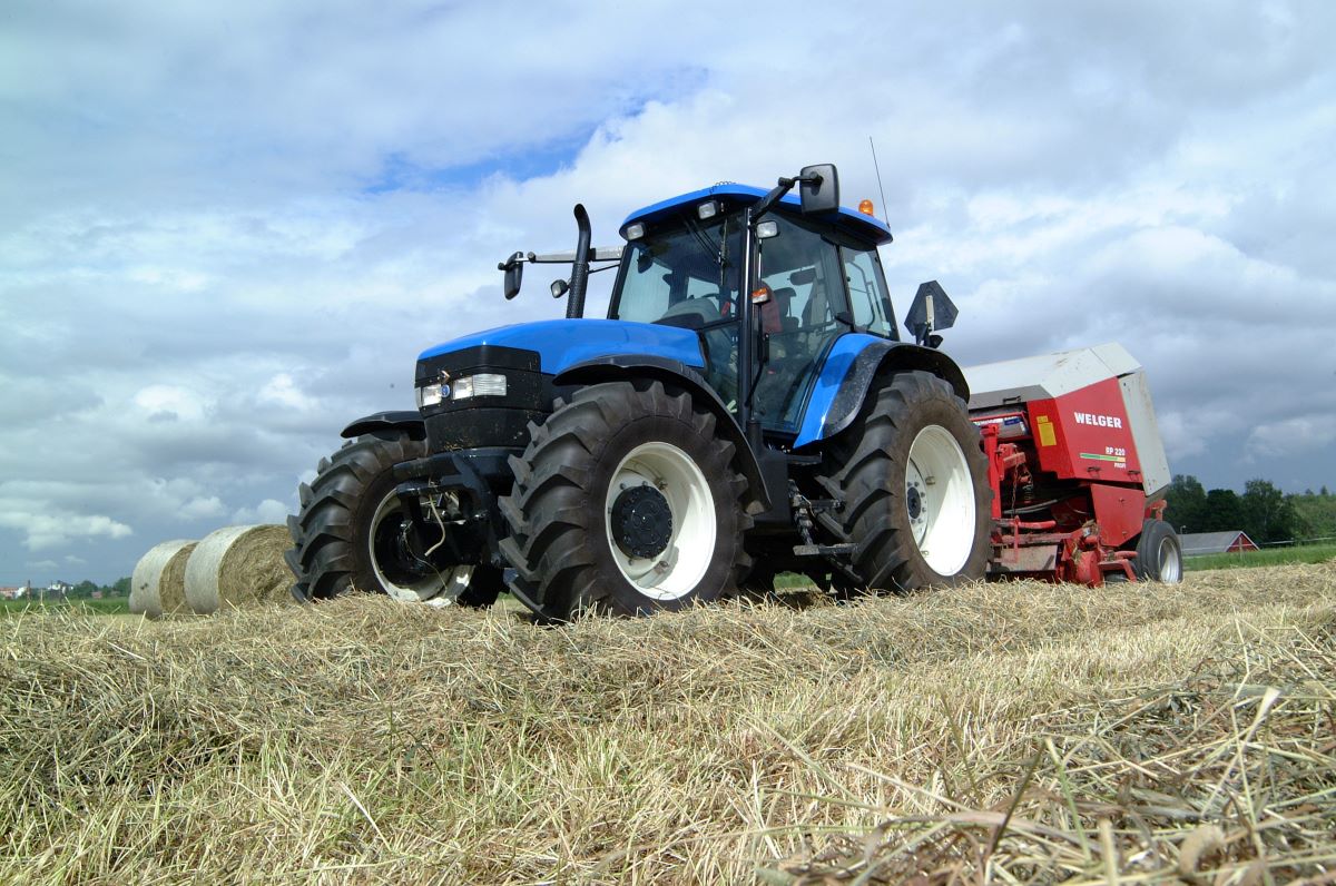 Traktor är på en höäng. Där finns stora höbalar.