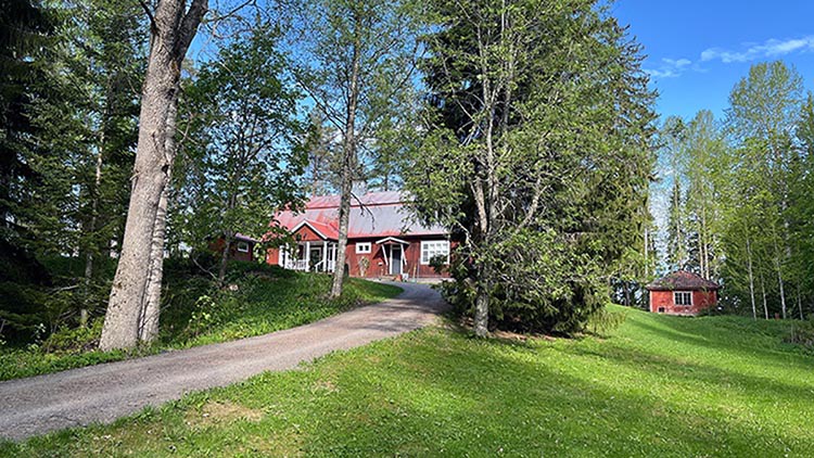 Bokhollarens rödfärgade hus syns bakom träden i parkliknande landskapet.